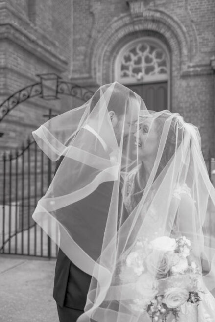 Groom lifting bride’s veil for a kiss in front of a historic New Orleans church.