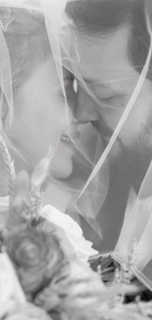 Close-up of bride and groom smiling under a veil with flowers during their New Orleans wedding.