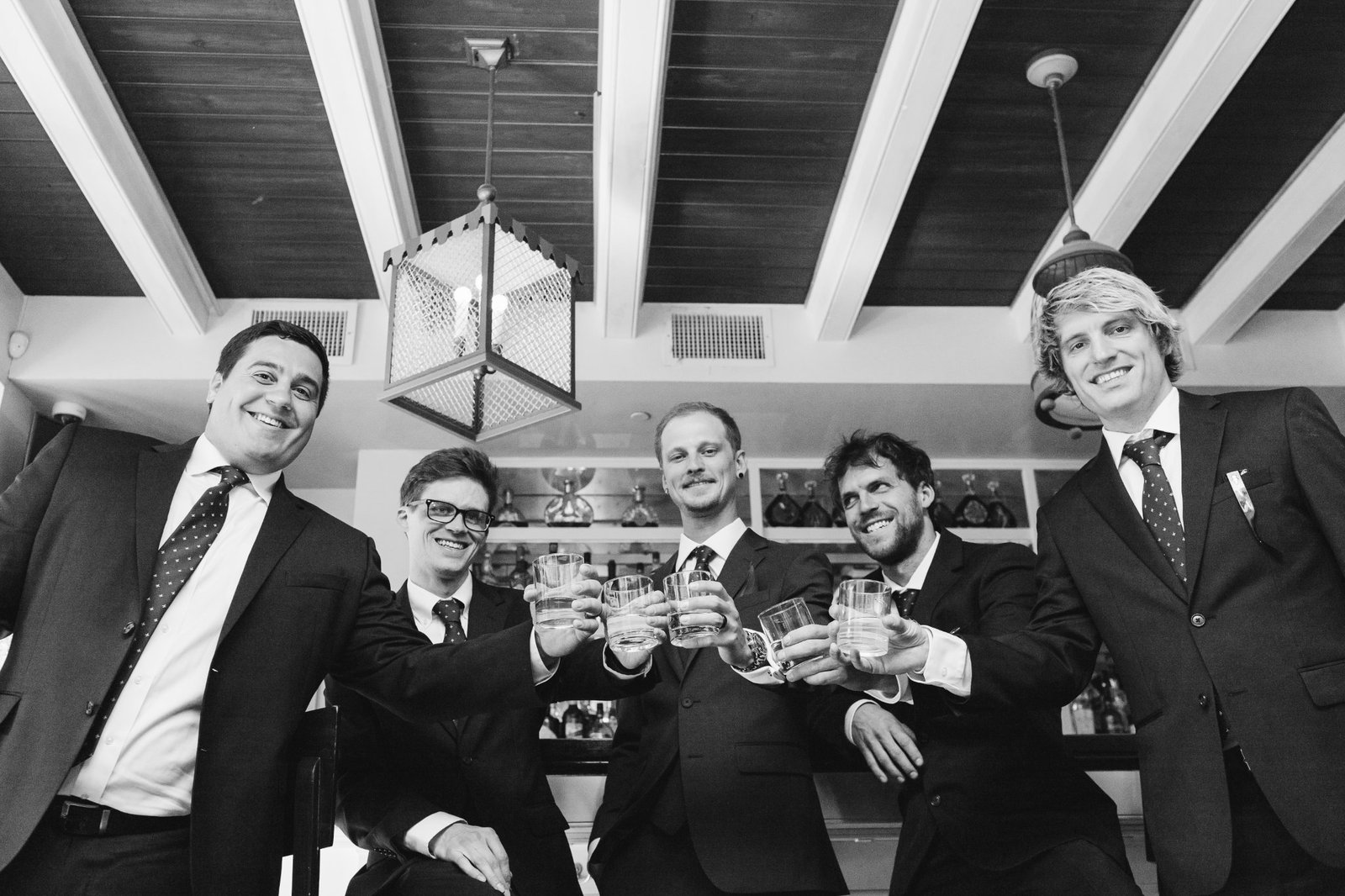 Groom and his friends clinking shot glasses at Brennan’s New Orleans before his elopement, captured in black and white.