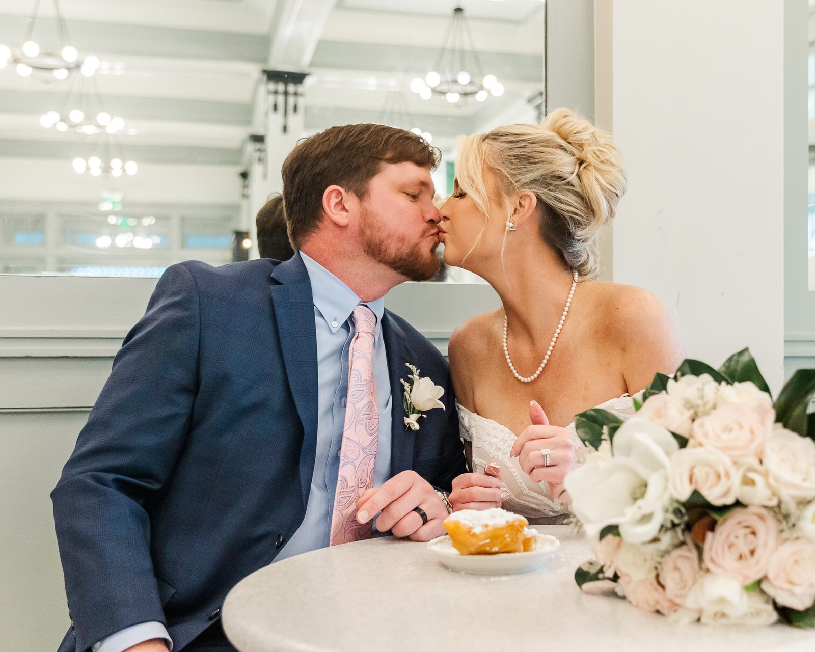 couple kissing while sharing beignets after eloping in New Orleans