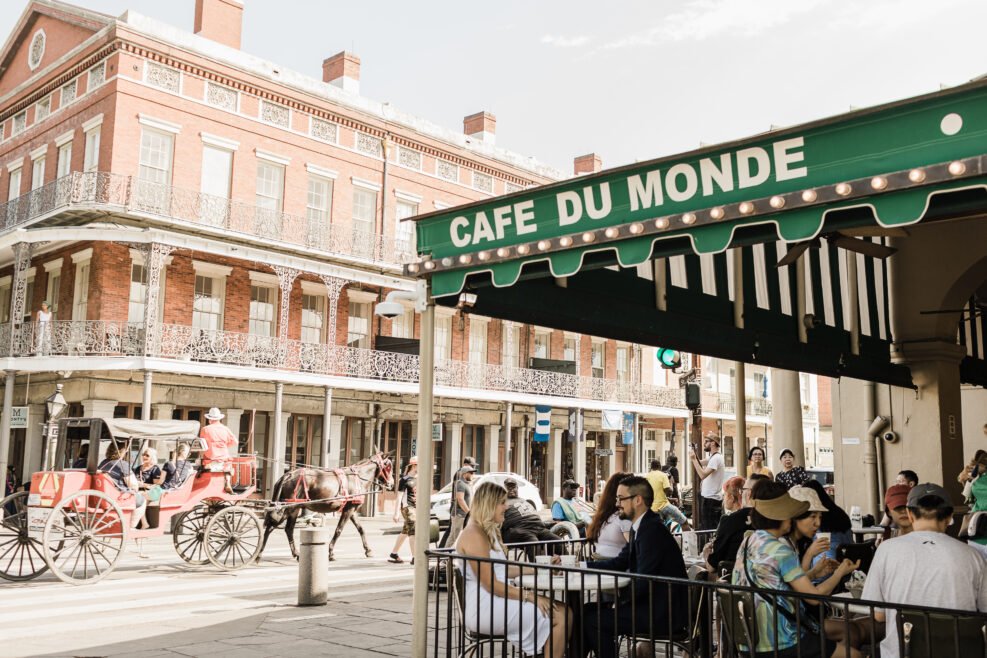 Couple enjoying a sweet moment at Café du Monde in the French Quarter after their New Orleans elopement, with a horse-drawn carriage passing by.