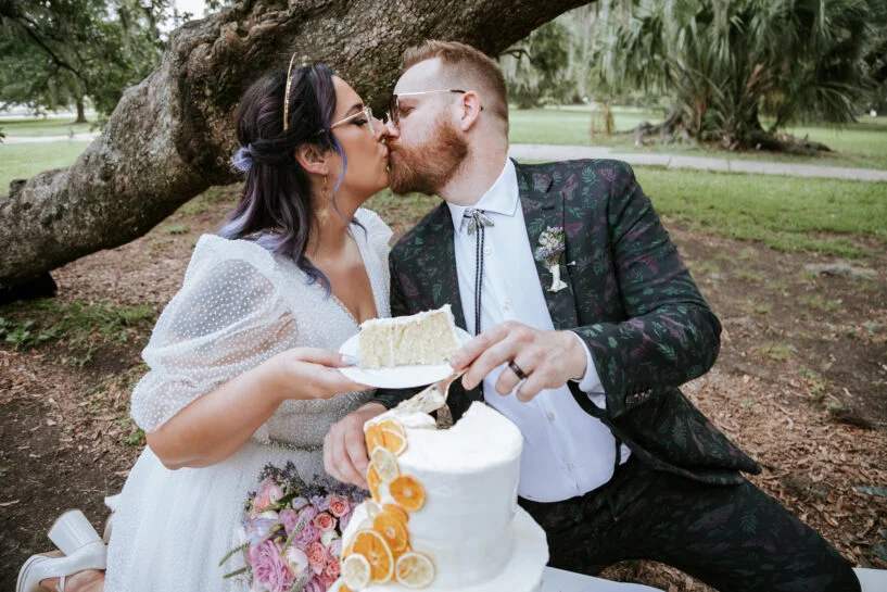 Couple shares a kiss behind their wedding cake after cutting it during their City Park elopement in New Orleans.