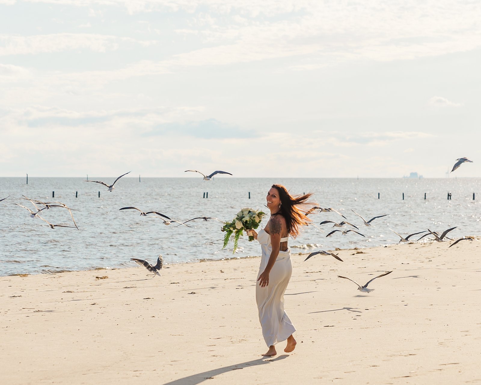 bride running into seagulls on the beach in Biloxi for her elopement