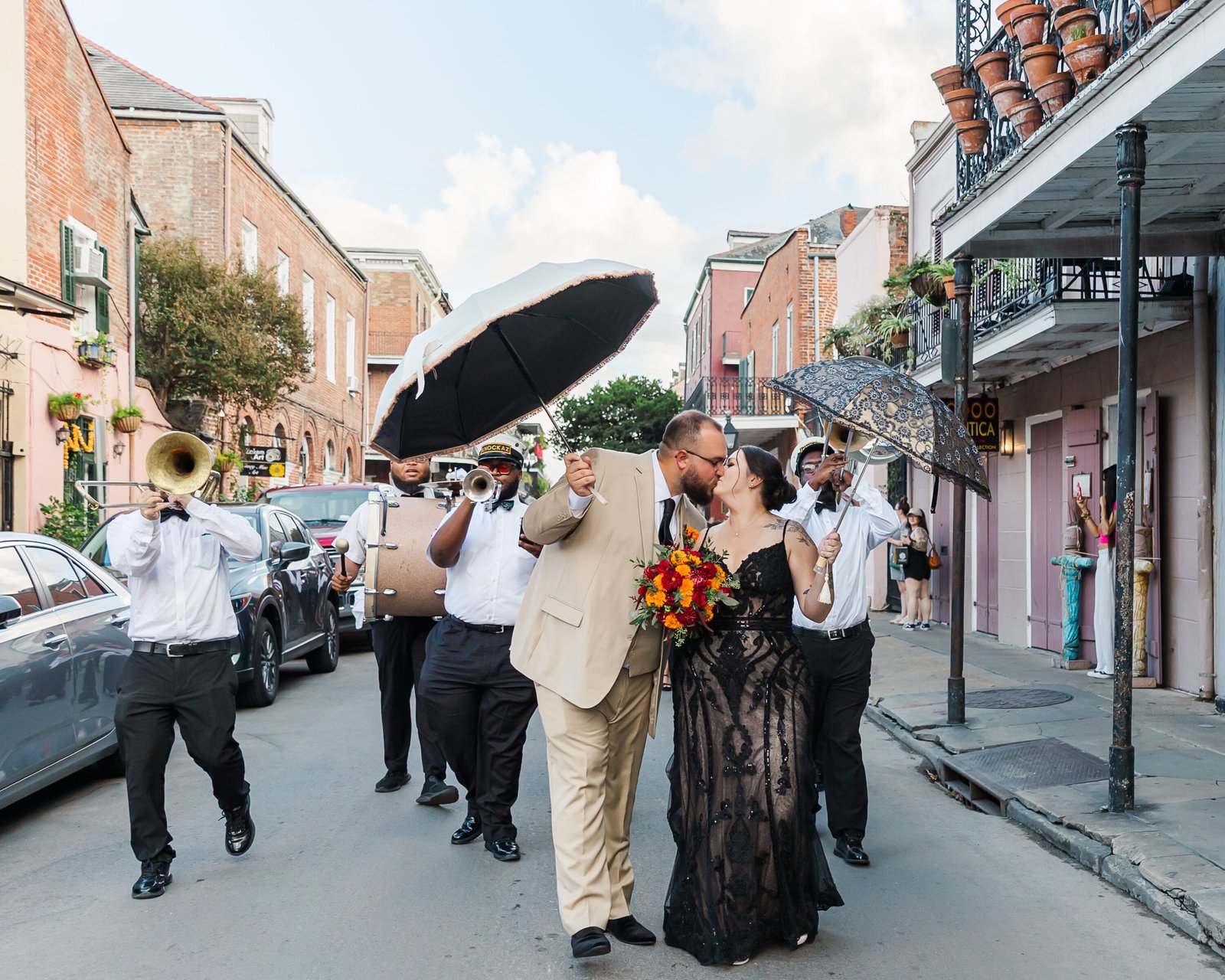 bride in black dress and groom with umbrella sharing a kiss in French quarter for their New Orleans elopement 2nd line