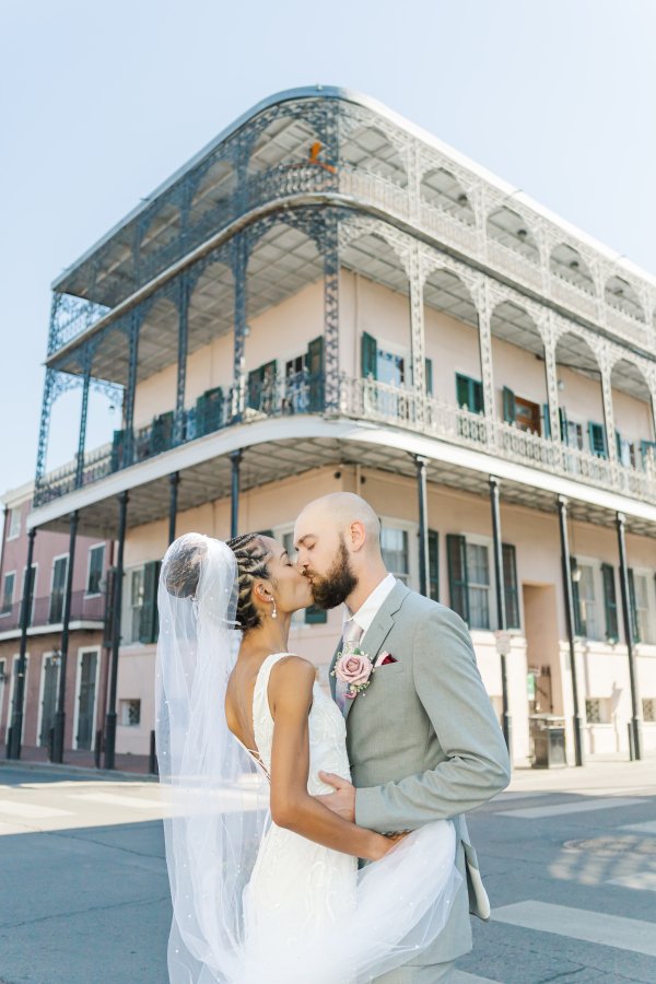 Cinematic kiss between an elopement couple on a historic New Orleans street corner framed by ornate cast-iron balconies.