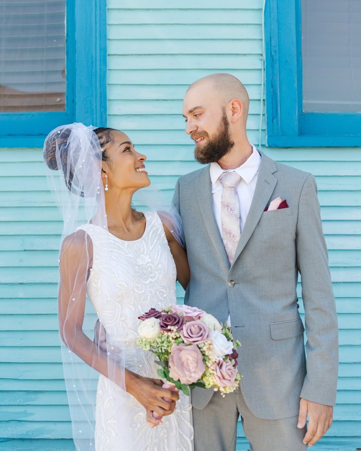Bride and groom standing in front of a historic French Quarter building in New Orleans with pink walls and traditional green shutters.